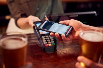 Close Up Of Man Paying For Drinks At Bar Using Contactless App On Mobile Phone