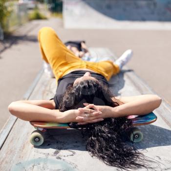 Young Woman Lying On Skateboard In Urban Skate Park