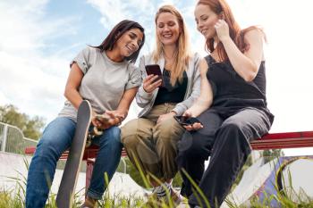 Group Of Female Friends With Skateboard Using Mobile Phones In Urban Skate Park
