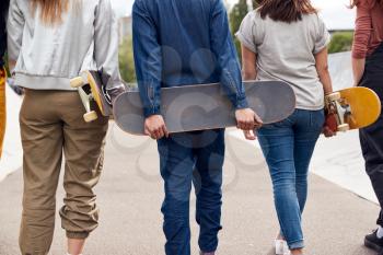 Rear View Of Female Friends With Skateboards Walking Through Urban Skate Park