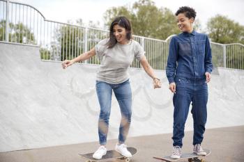 Two Female Friends Riding On Skateboards In Urban Skate Park