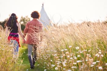 Young Romantic Couple Walking Through Field Towards Teepee On Summer Camping Vacation