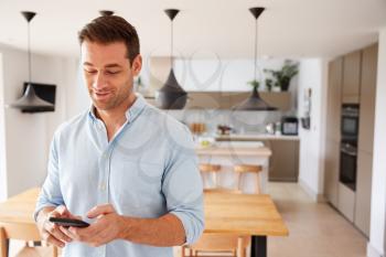 Man Using App On Smart Phone To Control Central Heating Temperature In House