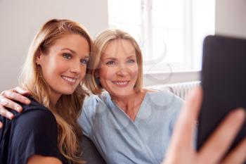Senior Mother With Adult Daughter Sitting On Sofa Posing For Selfie On Mobile Phone