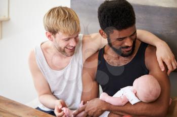Loving Male Same Sex Couple Cuddling Baby Daughter At Home Together