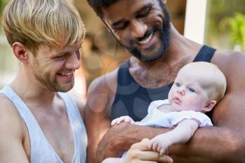 Loving Male Same Sex Couple Cuddling Baby Daughter At Home In Garden Together