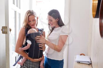Same Sex Female Couple With Baby Daughter In Sling Opening Front Door Of Home