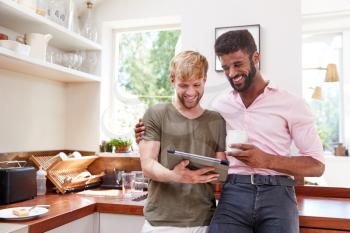 Male Gay Couple Using Digital Tablet At Home In Kitchen Together