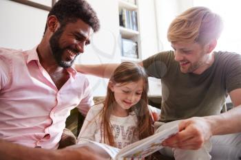 Same Sex Male Couple Reading Book With Daughter At Home Together Whilst Tickling Her