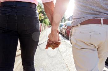 Close Up View Of Same Sex Male Couple Holding Hands As They Walk Along Road From Behind
