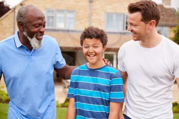 Father With Son And Grandfather From Multi-Generation Mixed Race Family Walking In Garden At Home