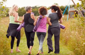 Rear View Of Mature Female Friends On Outdoor Yoga Retreat Walking Along Path Through Campsite