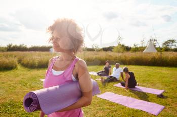 Mature Woman On Outdoor Yoga Retreat With Friends And Campsite In Background