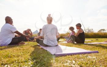 Female Teacher Leading Group Of Mature Men And Women In Class At Outdoor Yoga Retreat