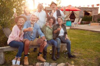 Portrait Of Mature Friends Sitting Around Fire And Making A Toast At Outdoor Campsite Bar