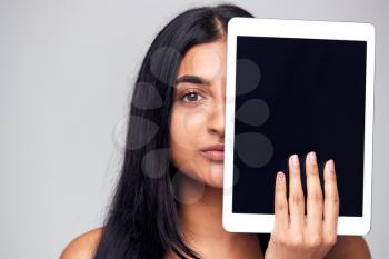 Studio Portrait Of Serious Young Woman Covering Face With Digital Tablet