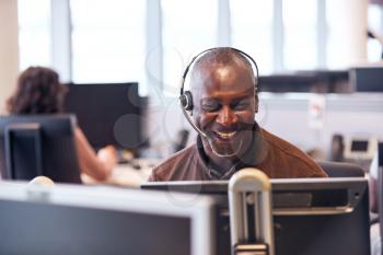 Mature Businessman Wearing Telephone Headset Talking To Caller In Customer Services Department