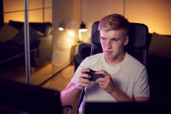 Teenage Boy With Game Pad Sitting In Chair and Gaming At Home