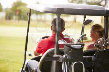 Rear View Of Couple Playing Golf Driving Buggy Along Fairway On Red Letter Day