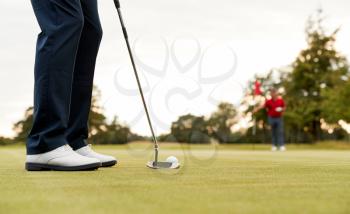 Close Up Of Female Golfer Putting Ball On Green As Man Tends Flag