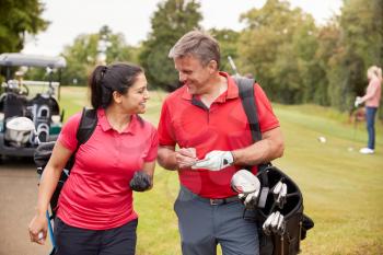 Mature Couple Playing Round Of Golf Carrying Golf Bags And Marking Scorecard