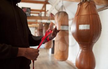 Close Up Of Male Boxer Training In Gym Putting Wraps On Hands Standing Next To Punching Bag
