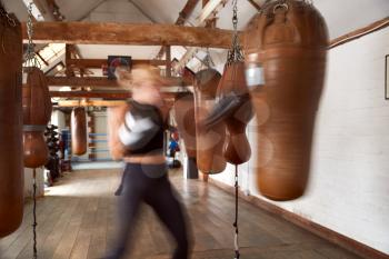 Action Shot Of Male And Female Boxers In Gym Training With Leather Punch Bags