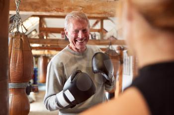 Senior Male Boxer Sparring With Younger Female Coach In Gym Using Training Gloves
