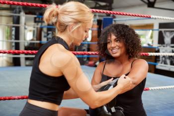 Personal Trainer Helping Female Boxer In Gym To Put On Boxing Gloves In Gym