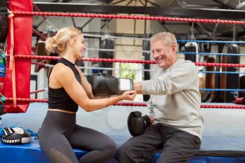 Personal Trainer Helping Senior Male Boxer In Gym To Put On Boxing Gloves In Gym