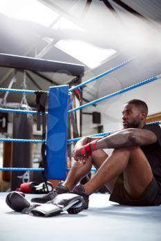 Tired Male Boxer Sitting In Boxing Ring In Gym After Training Session
