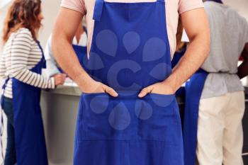 Close Up Of Man With Hands In Apron Pocket Taking Part In Cookery Class In Kitchen