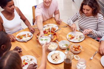 Group Of Friends Sitting Around Table Eating Meal At Home Together