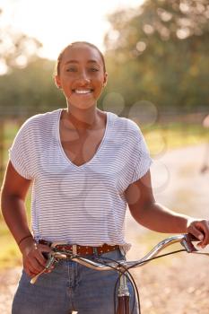 Portrait Of Young Woman Riding Bike Along Country Lane At Sunset