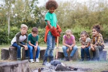Group Of Children On Outdoor Activity Camping Trip Cooking Over Camp Fire Together