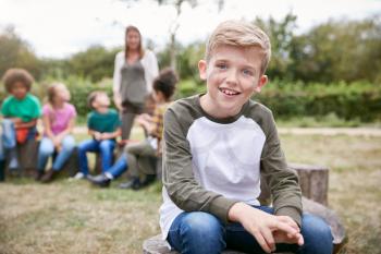 Portrait Of Boy On Outdoor Activity Camping Trip Sitting Around Camp Fire With Friends