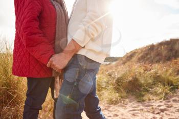 Close Up Of Loving Senior Couple Holding Hands Walking Through Sand Dunes On Winter Vacation