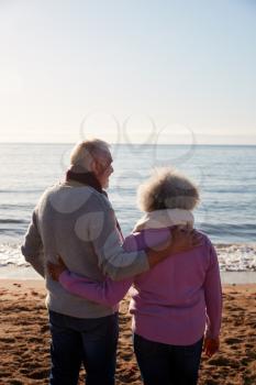 Rear View Of Loving Retired Couple Hugging Standing Looking Out To Sea On Winter Beach Vacation