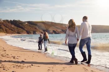 Rear View Of Family With Fishing Nets Walking Along Shoreline Of Winter Beach