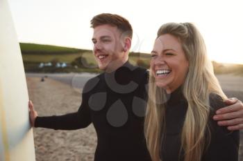 Young Couple Wearing Wetsuits Enjoying Surfing Staycation On Beach As Sun Sets