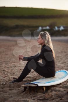 Side View Of Thoughtful Woman Wearing Wetsuit On Surfing Staycation Looking Out To  Sea At Waves