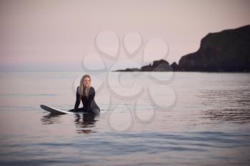 Woman Wearing Wetsuit Sitting And Floating On Surfboard On Calm  Sea