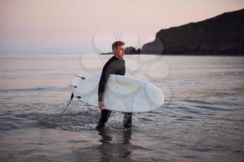 Man Wearing Wetsuit Carrying Surfboard As He Walks Out Of Sea