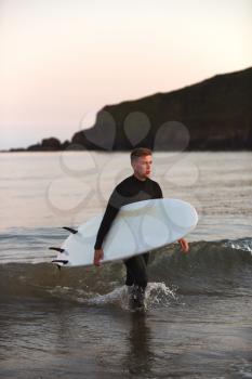 Man Wearing Wetsuit Carrying Surfboard As He Walks Out Of Sea