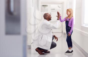 Male Paediatric Doctor Giving Young Girl Patient High Five In Hospital Corridor