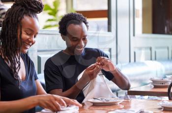 Male And Female Waiters Folding Napkins In Restaurant Before Service