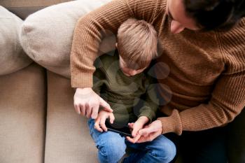 Father And Son On Sofa At Home Having Fun Playing Game On Mobile Phone