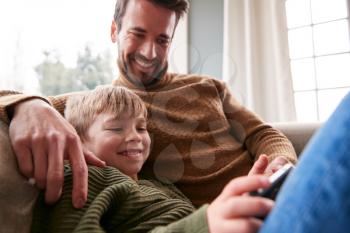 Father And Son On Sofa At Home Having Fun Playing Game On Mobile Phone