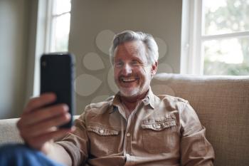 Mature Man At Home Self Isolating During Lockdown Making Video Call On Mobile Phone