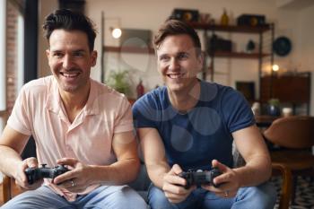 Loving Same Sex Male Couple Sitting On Sofa At Home Gaming Together